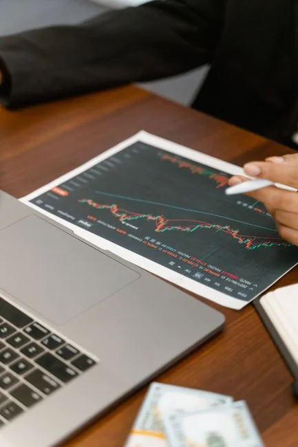 Business professionals analyzing stock charts and graphs on a laptop in an office setting.
