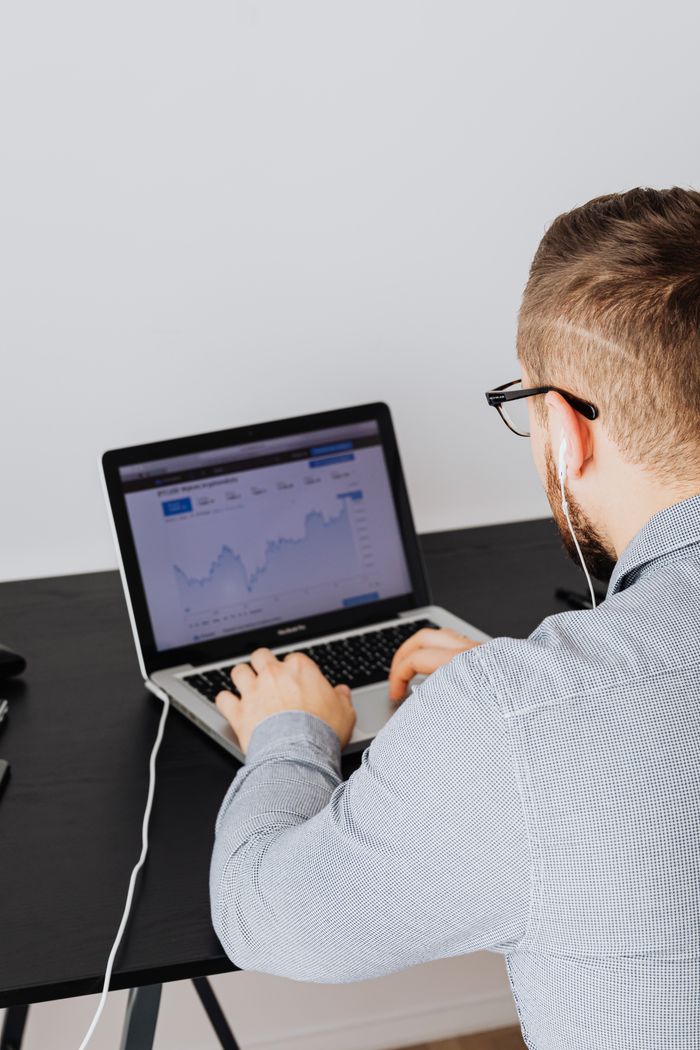 A man is using a laptop indoors to review stock market trend graphs displayed on the screen.